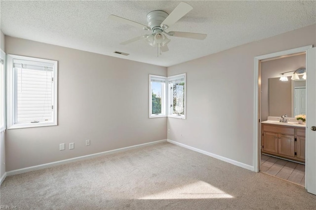 unfurnished bedroom with visible vents, baseboards, ensuite bathroom, a textured ceiling, and light colored carpet