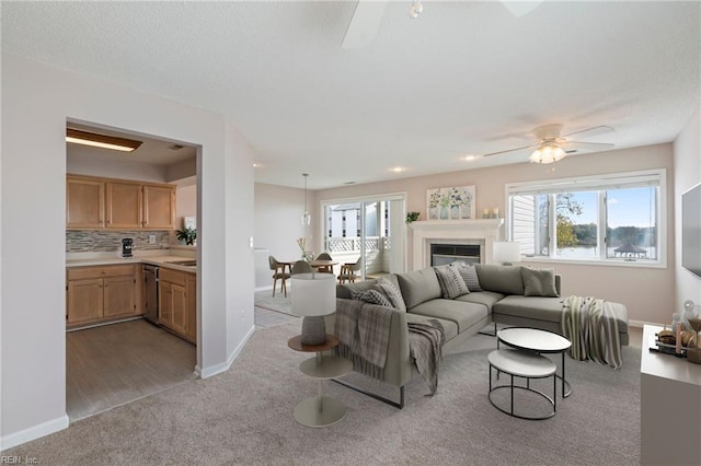 living room with light carpet, a glass covered fireplace, baseboards, and a ceiling fan