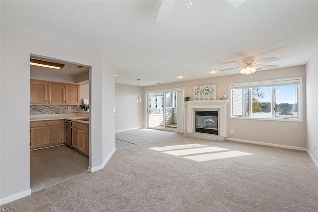 unfurnished living room with light carpet, a textured ceiling, a fireplace, baseboards, and ceiling fan