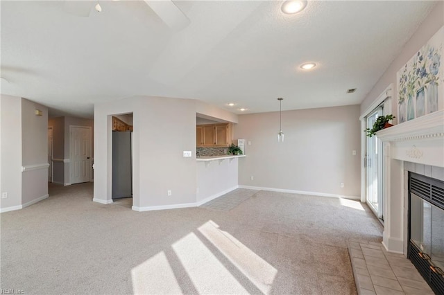 unfurnished living room with light carpet, recessed lighting, a tile fireplace, and baseboards