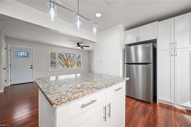 kitchen featuring light stone counters, a ceiling fan, freestanding refrigerator, dark wood-type flooring, and white cabinets