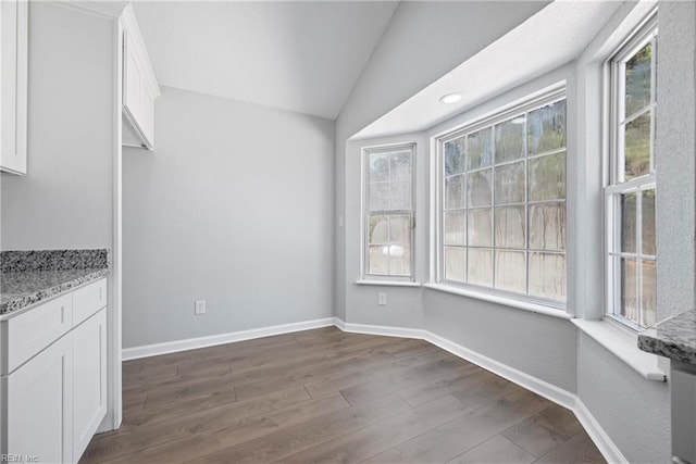 unfurnished dining area with vaulted ceiling, baseboards, and dark wood-type flooring