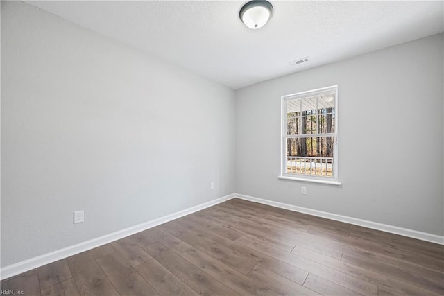 empty room featuring dark wood finished floors, visible vents, a textured ceiling, and baseboards