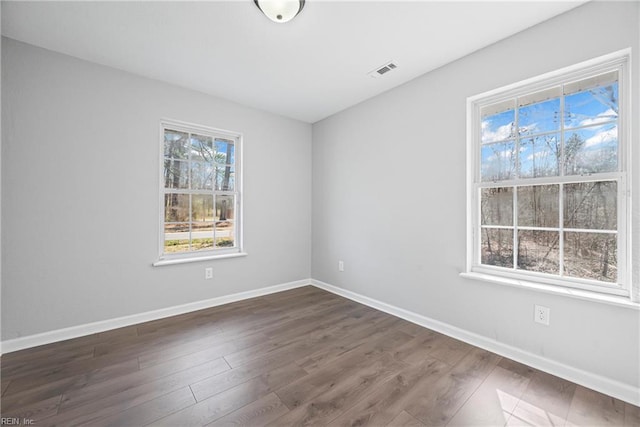 empty room featuring visible vents, baseboards, and dark wood-style floors