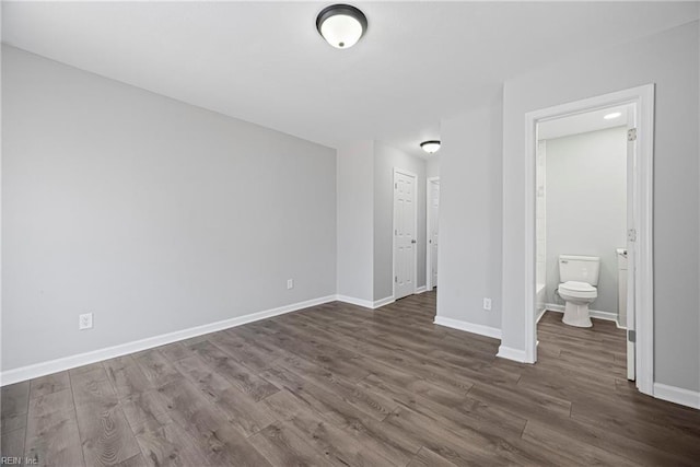 unfurnished bedroom with baseboards, dark wood-type flooring, and ensuite bathroom