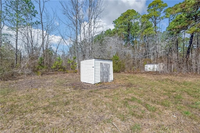 view of yard featuring a view of trees, a storage shed, and an outdoor structure