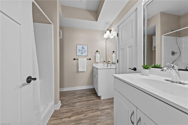 full bathroom featuring wood finished floors, baseboards, two vanities, a sink, and a shower