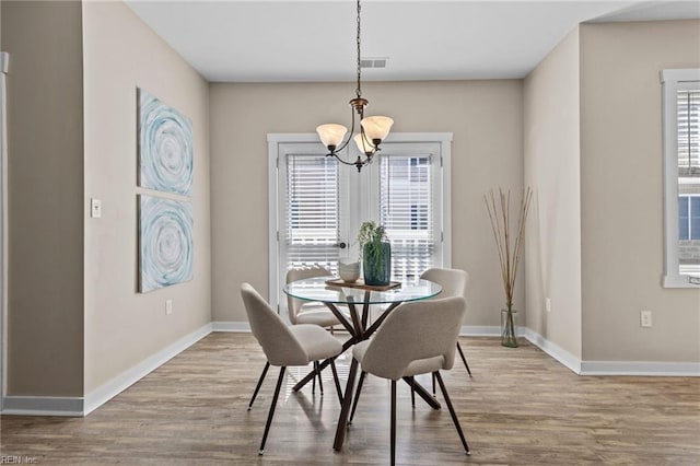 dining area featuring a chandelier, baseboards, visible vents, and wood finished floors