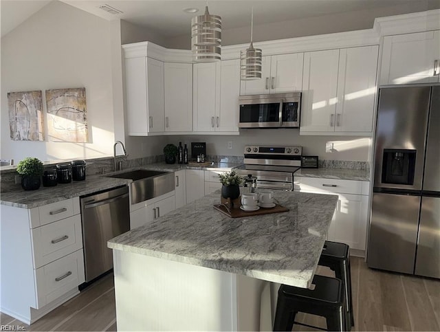 kitchen with visible vents, a center island, appliances with stainless steel finishes, wood finished floors, and a sink