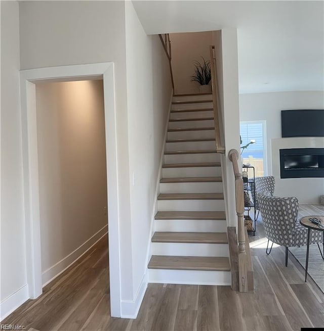 stairway with a glass covered fireplace, baseboards, and wood finished floors