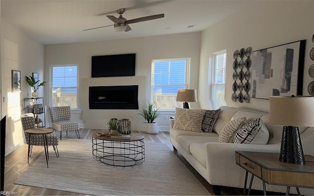 living area featuring ceiling fan, a healthy amount of sunlight, wood finished floors, and a fireplace