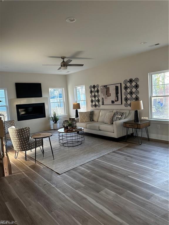 living room with visible vents, a ceiling fan, wood finished floors, a glass covered fireplace, and baseboards