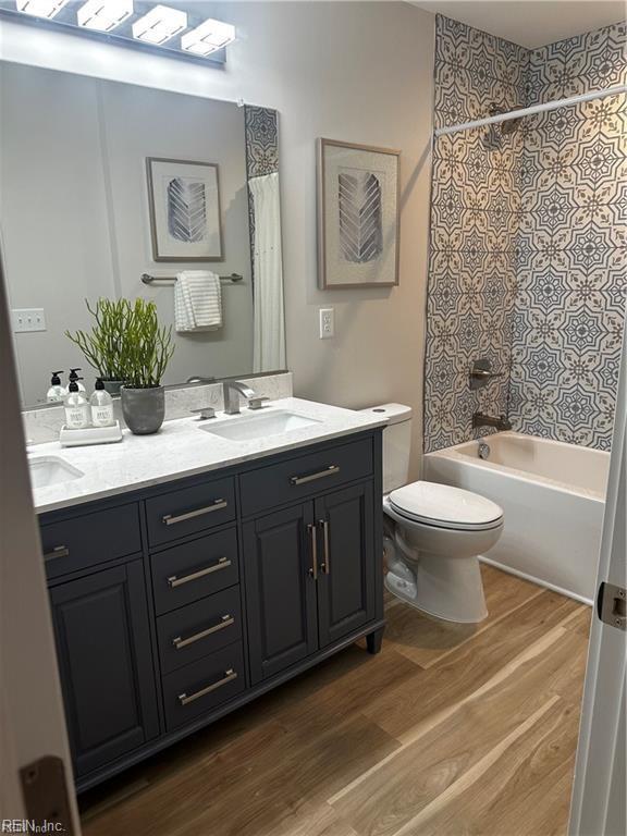 full bath with shower / tub combo with curtain, toilet, a sink, wood finished floors, and double vanity