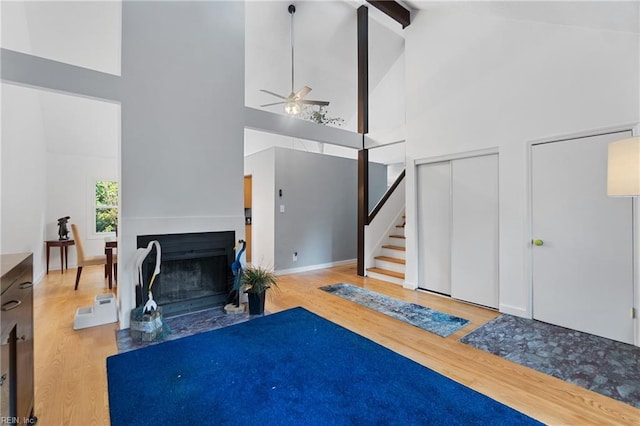 living area with a fireplace with flush hearth, beamed ceiling, stairway, and wood finished floors