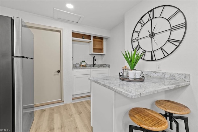 kitchen with light wood finished floors, a kitchen breakfast bar, freestanding refrigerator, white cabinets, and open shelves