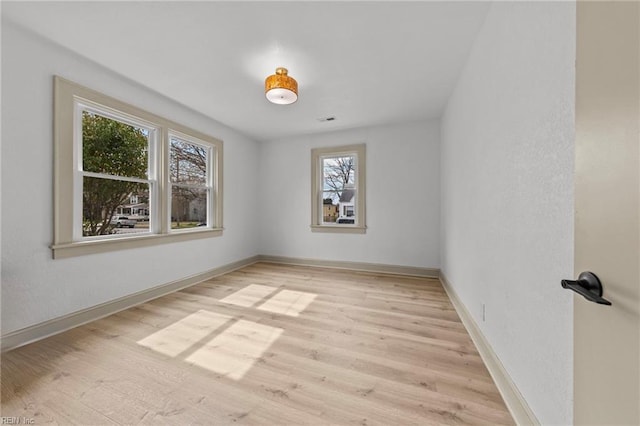 empty room with light wood-style flooring, visible vents, and baseboards