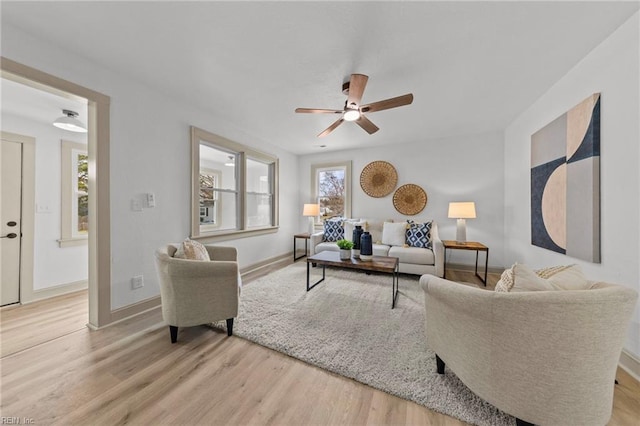 living area featuring light wood-type flooring, baseboards, and ceiling fan