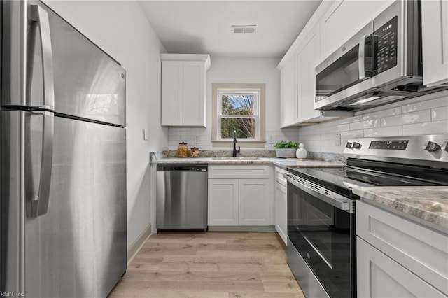 kitchen with visible vents, light wood-style flooring, appliances with stainless steel finishes, white cabinets, and a sink