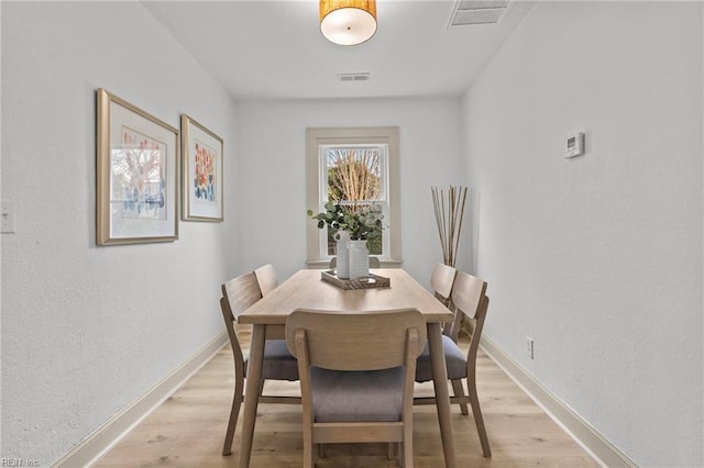 dining area with light wood-type flooring, visible vents, and baseboards