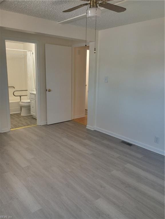 unfurnished bedroom featuring wood finished floors, baseboards, visible vents, a textured ceiling, and connected bathroom