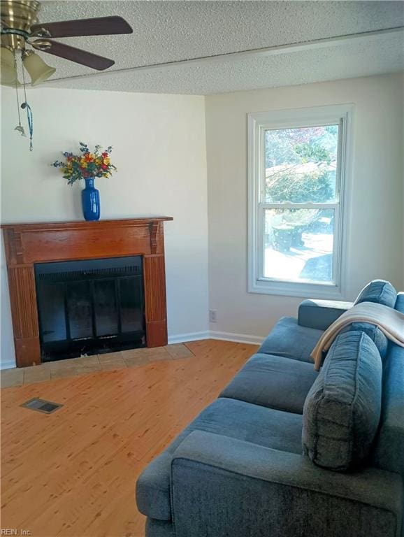 living room featuring visible vents, baseboards, a fireplace with flush hearth, wood finished floors, and a textured ceiling