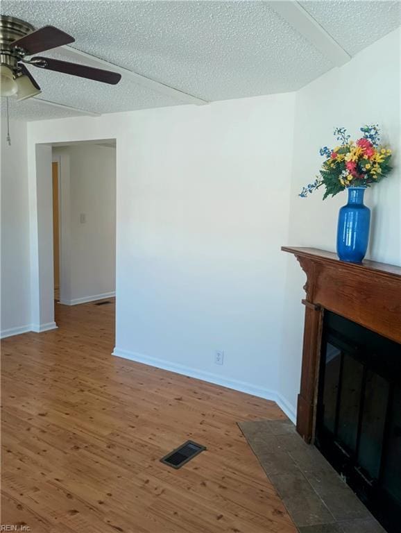 unfurnished living room featuring visible vents, a fireplace with flush hearth, a textured ceiling, and wood finished floors