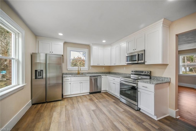 kitchen featuring white cabinetry, light stone counters, appliances with stainless steel finishes, and a sink