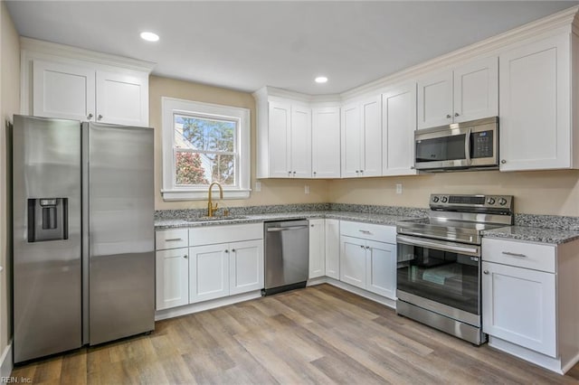 kitchen with a sink, stainless steel appliances, white cabinets, light wood finished floors, and light stone countertops