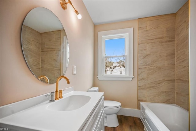 bathroom featuring baseboards, a washtub, toilet, wood finished floors, and vanity