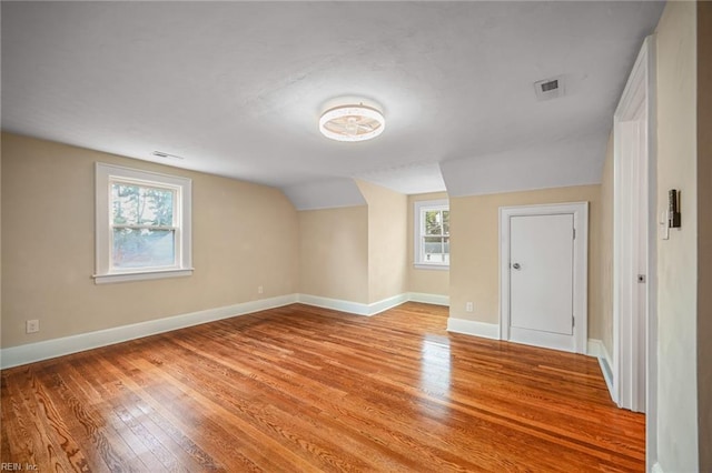 unfurnished room featuring vaulted ceiling, light wood-style floors, baseboards, and visible vents