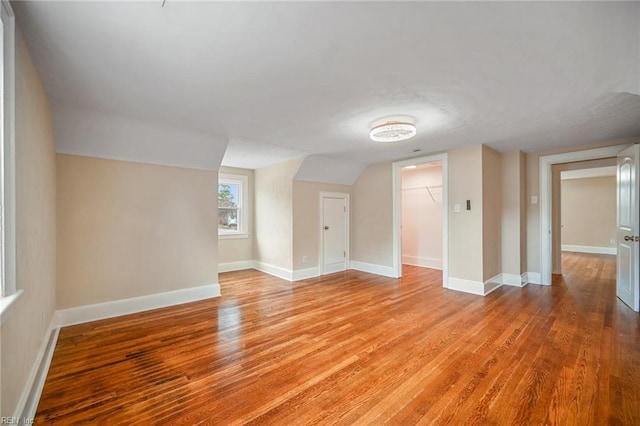 empty room featuring light wood finished floors, lofted ceiling, and baseboards