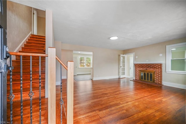 unfurnished living room featuring a brick fireplace, stairway, wood finished floors, and baseboards