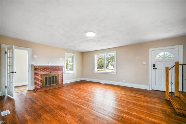 unfurnished living room with visible vents, a brick fireplace, baseboards, stairs, and wood finished floors