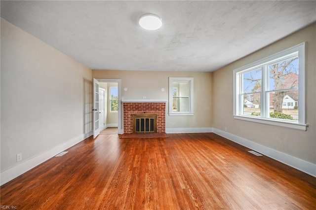 unfurnished living room with a brick fireplace, wood finished floors, visible vents, and baseboards