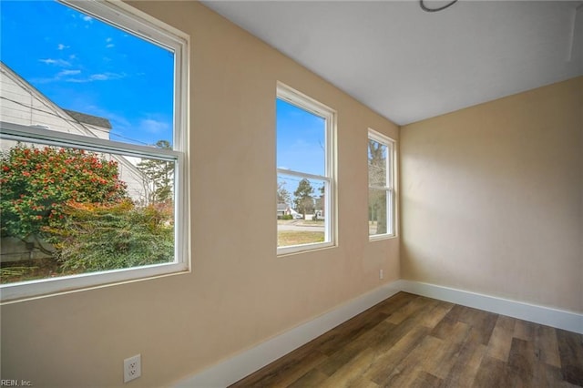 empty room featuring dark wood-style floors, a healthy amount of sunlight, and baseboards