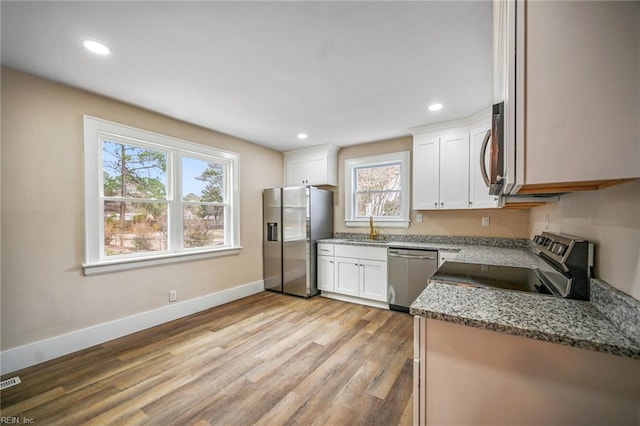 kitchen featuring light wood finished floors, baseboards, light stone countertops, white cabinets, and stainless steel appliances