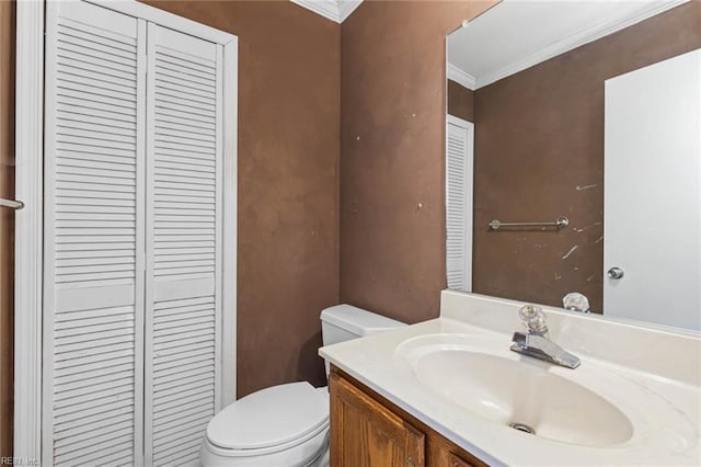 half bath featuring a closet, toilet, ornamental molding, and vanity