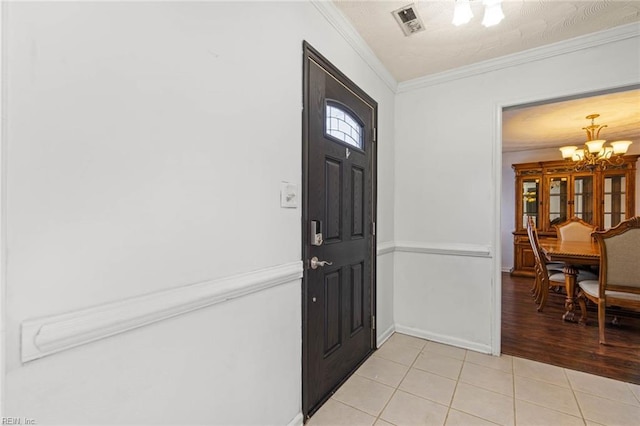 foyer entrance with visible vents, baseboards, light tile patterned flooring, crown molding, and a notable chandelier