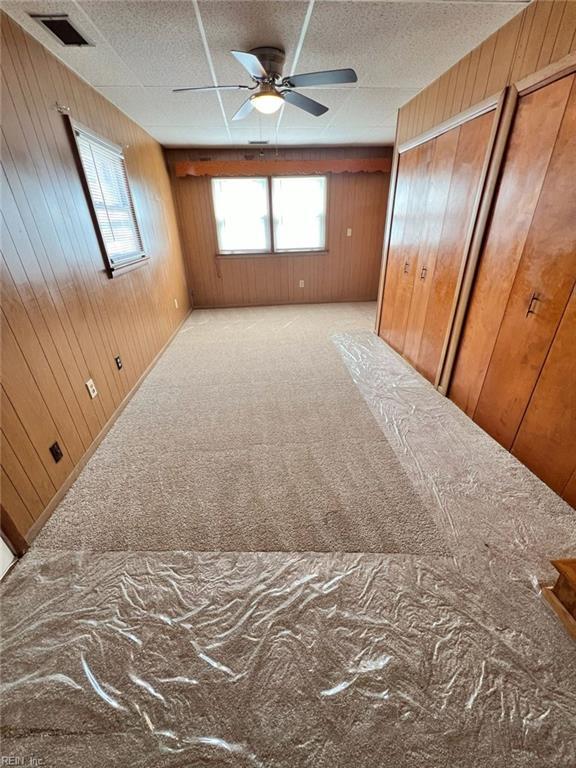 unfurnished bedroom with visible vents, carpet flooring, a ceiling fan, and wooden walls