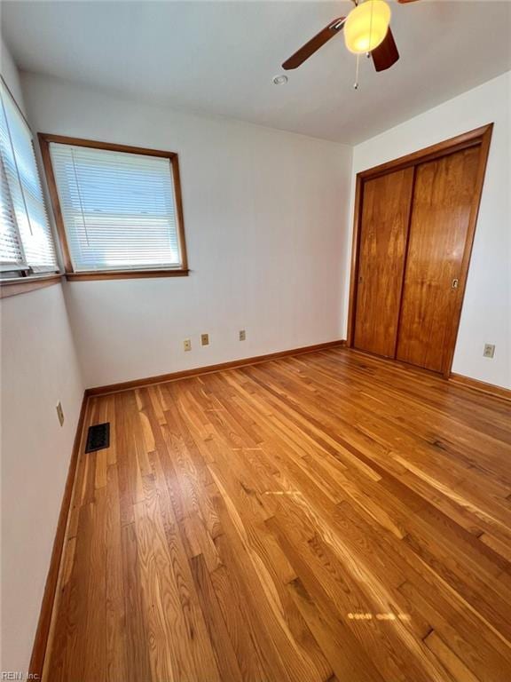 unfurnished bedroom with baseboards, visible vents, light wood finished floors, ceiling fan, and a closet