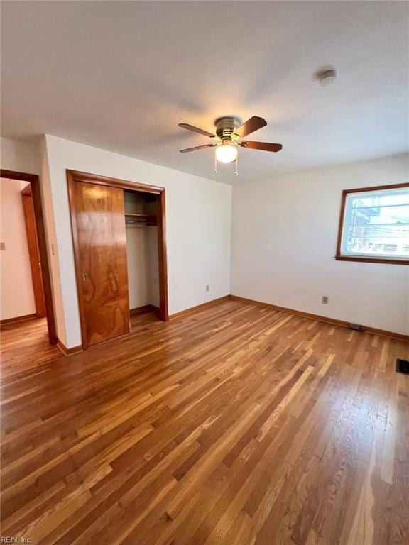 unfurnished bedroom with ceiling fan, wood finished floors, a closet, and baseboards