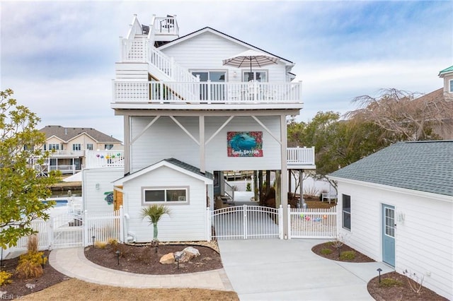 rear view of house with stairway, a gate, fence, concrete driveway, and a carport