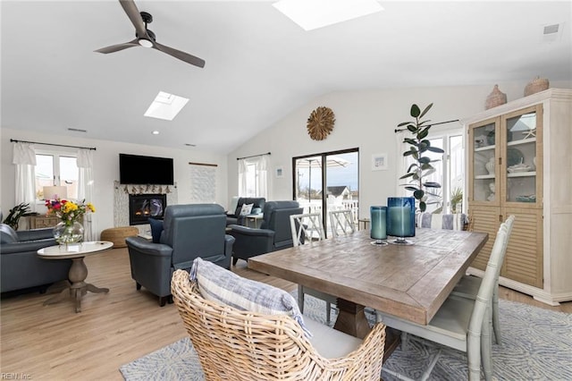 dining room featuring vaulted ceiling with skylight, light wood-style floors, a glass covered fireplace, and a ceiling fan