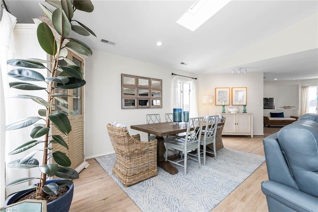 dining space with light wood finished floors, visible vents, baseboards, vaulted ceiling with skylight, and recessed lighting