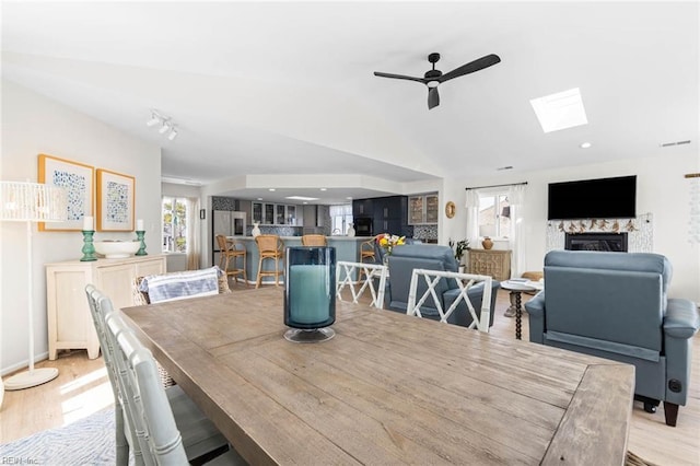 dining space featuring lofted ceiling with skylight, light wood finished floors, a fireplace, and ceiling fan