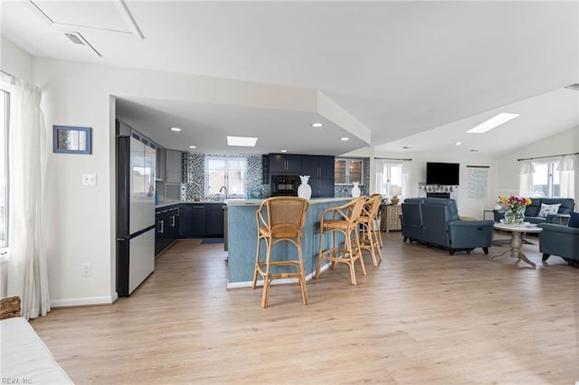 kitchen with open floor plan, a breakfast bar area, light wood-type flooring, light countertops, and fridge