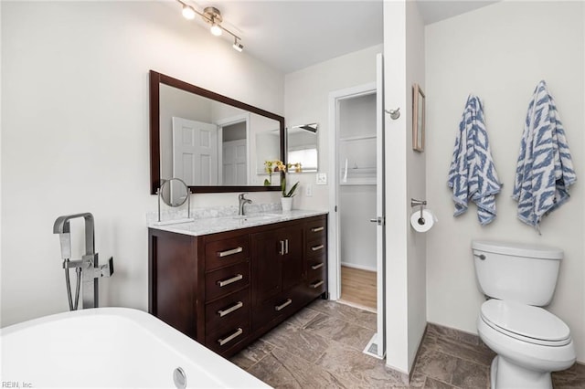 bathroom with a freestanding tub, baseboards, toilet, and vanity