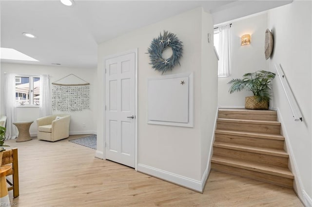 hall with baseboards, stairs, recessed lighting, light wood-style flooring, and a skylight