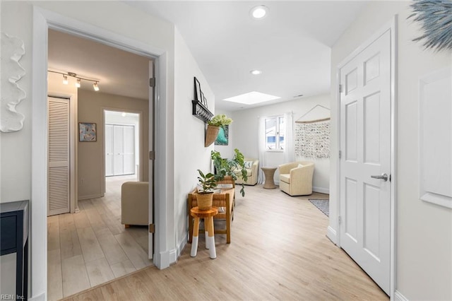 hall with a skylight, recessed lighting, light wood-style flooring, and baseboards