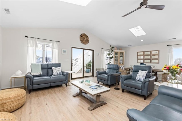 living room featuring ceiling fan, vaulted ceiling with skylight, visible vents, and light wood-type flooring